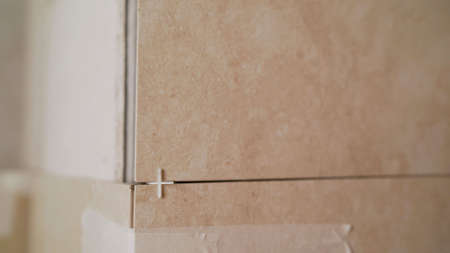 Close-up view of tiler hands fixing wall tile with spacers at home repair renovation work. Laying...