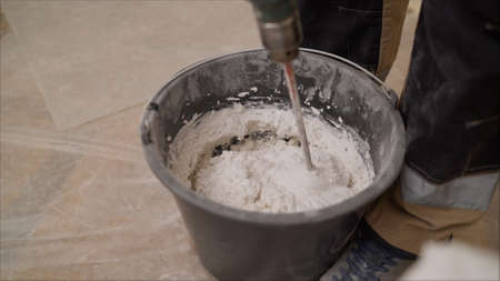 Mix the mixture in a black bucket. Worker mixes a solution in a black bucket. A man mixes a white...