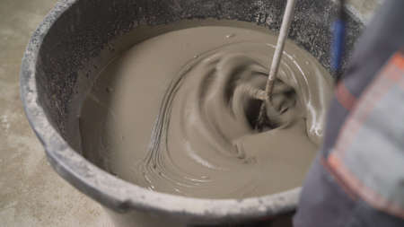 A worker mixes the solution in a bucket. The mortar is mixed with a construction mixer. Floor renovation process.の写真素材