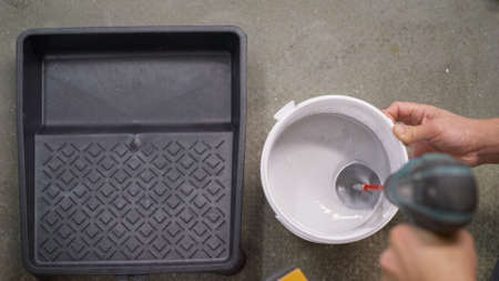 The white paint is mixed in a bucket with a drill. Drill paddle mixer on a bucket with white paint,...