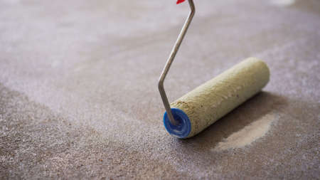 A worker applies the primer to the concrete floor with a roller. Applying a primer to the floor. Floor priming. worker brush primer grout of stonesの写真素材