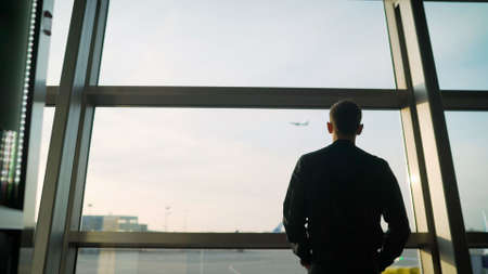 A respectable young man stands at the airport and looks at the plane. Young guy at the airport. The...