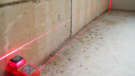 Setting the laser level on the wall. Close-up of modern engineering device set on the floor,...