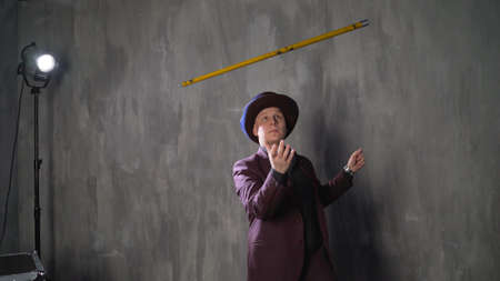 Magician - the appearance of a stick from a scarf. Illusionist is doing magic trick in slow motion. Magician man in black suit is showing trick doing metal stick from headscarf and looking at camera. Concept of performances, shows and circus.の写真素材