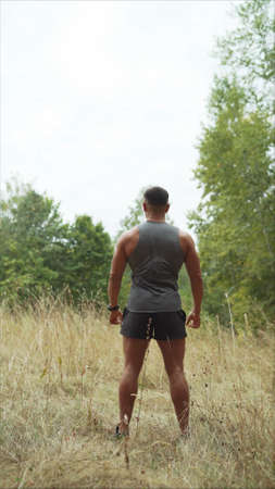 A handsome, hard-working man is standing in a field. Athlete in the forest.