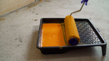 Orange putty and roller in the tray. Putty, tray and roller. Paint roller, tray with orange paint on concrete floor background. Renovation of the wall in the room.の写真素材
