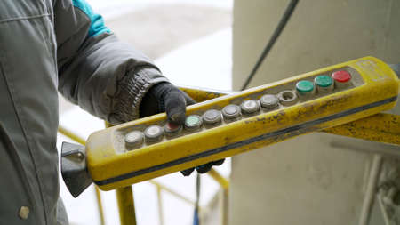 Male hand push remote control switch for overhead crane in the factory, close-up. Electrical control...