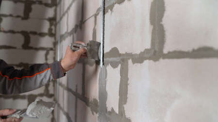 A professional bricklayer-builder by a manual craftsman applies cement mortar to the primed wall. A worker applies plaster to the wall with a trowel.の写真素材