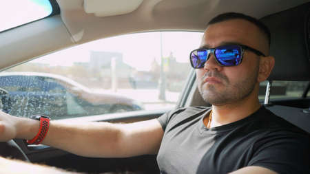 The brutal guy is sitting in the car, talking on the phone and smoking. The tough guy is talking on the phone while sitting in the car. close up photo side view. conversation, technology concept.の写真素材