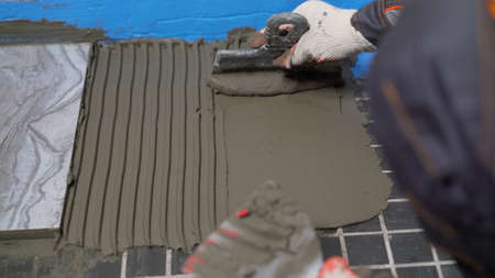 Applying adhesive solution to the tile floor. Builder smears the solution on the tile.