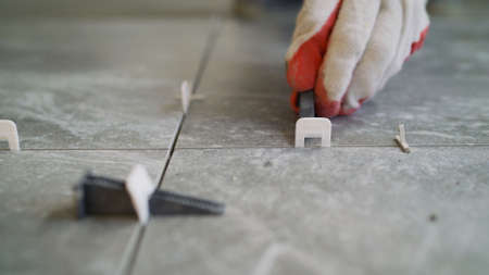 Laying tiles on the floor. The man is installing ceramic tiles. For fixing at the same distance. Installation of the luminaire on floor tiles.の写真素材