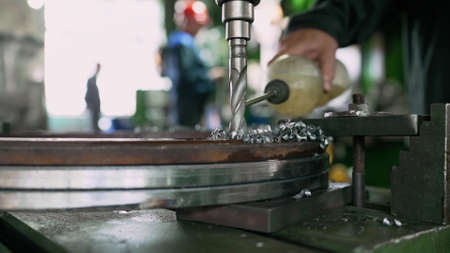 A metal drill makes holes in a metal product on an industrial drilling machine with shavings....