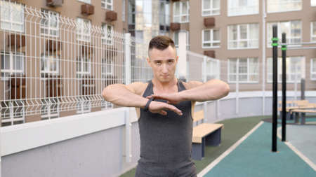 The athlete is doing exercises on the sports field on the street. Man warming up.