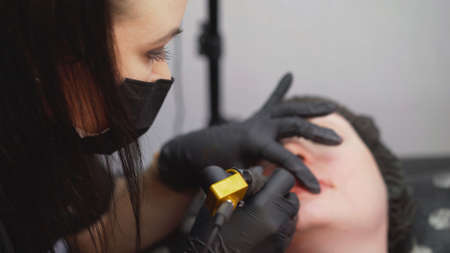 Tattooing the lips. Close up of permanent lip makeup. lip tattoo. The master is engaged in tattooing lips and eyes.の写真素材