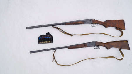 Guns in the snow. The hunting weapon lies on the white snow. Preparing for winter hunting. Two weapons next to each other. The shotguns lie in the snow next to the cartridges.の写真素材