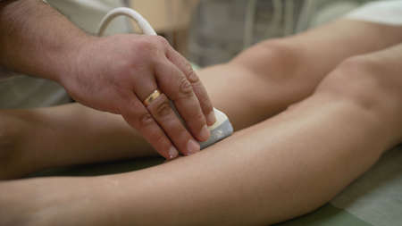 The doctor checks the veins in the patients legs with a machine. Doctor makes ultrasound of veins on patients legs, close up. Phlebologist uses an ultrasound machine to scan a patient.の写真素材