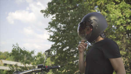 Brutal young man in sunglasses, blue sits on a custom motorcycle on the field with a black helmet....