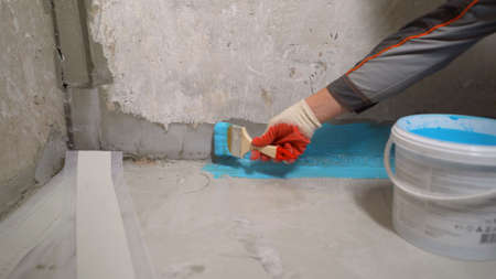 A worker applies waterproofing paint to the bathroom wall and floor. Applying waterproofing in the bathroom.の写真素材