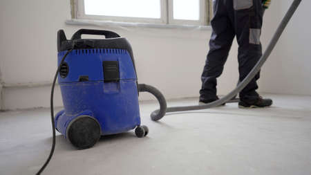 Worker washes the floor with a vacuum cleaner from industrial concrete dust and cement mud during home renovation. A worker vacuums a concrete floor.の写真素材
