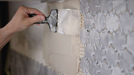 Close-up of a hand applying a ceramic tile adhesive. Close-up of ceramic tiles with glue on the...