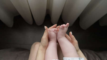 Baby feet in mother hands. Tiny Newborn Babys feet on female Shaped hands closeup. Mom and her...