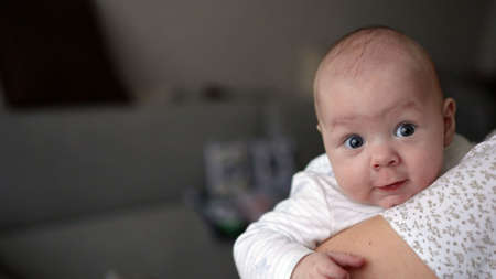 Young woman mom with baby girl on hands near window at home. The baby in the arms of his mother smiles.の写真素材