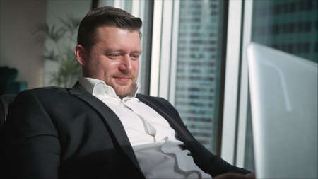 Successful businessman is resting while sitting in a chair behind a laptop. Surfing web at home....