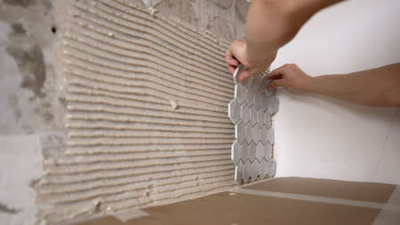 The hands of the master glue the mosaic tiles. Laying gray mosaic tiles by the hands of a master. Mosaic tile kitchen apron.の写真素材