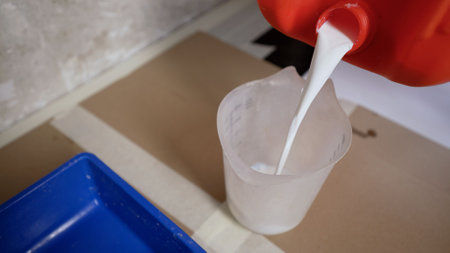 The primer is poured from the canister. Tray of paint with primer. A worker pours primer into a measuring cup. Preparation for painting work. Primer canister. Preparation for priming the plastered surface for further painting.の写真素材