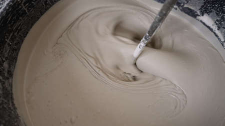 A worker using a mixer mixes the self-leveling floor in a bucket. Stir the solution in a bucket. Bricklayer mixes cement in a bucket. Preparation of a solution for plaster by mixing a mixture of water-based consistency. Self-leveling floor, cooking.の写真素材