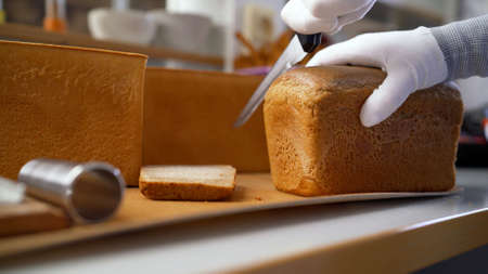 A woman cuts a loaf of bread in production. Woman cutting bread on wooden board. Bakehouse. Bread production.の写真素材