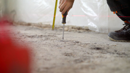 Installation of beacons on the floor. A worker drives a screw into the floor. Floor renovation concept. A worker's hand with a screwdriver is screwing a screw into a concrete floor.の写真素材