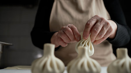 Person preparing traditional Georgian khinkali dumplings. Close-up, female hands making khinkali.の写真素材