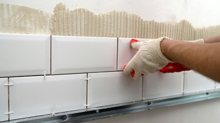 A worker lays and installs white ceramic tiles in a kitchen. Ceramic tile-fish. Laying ceramic tiles on the backsplash of the kitchen.の写真素材
