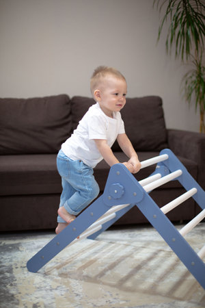 A cute kid performs gymnastic exercises on the stairs. Childrens sports wooden ladder. Physical education of children at home. The boy climbs the wooden stairs - at home.の写真素材