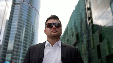 A successful businessman in a suit and sunglasses walks against the backdrop of skyscrapers. The concept of a successful businessman. The businessman goes near the skyscrapers.の写真素材