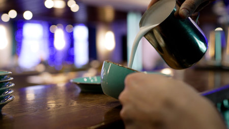 The barista pours milk into a cup. Barista pours cream into a cup of coffee. Small coffee business. Favorite job in the restaurant industry. Close-up of barista's hands making latte art coffee.の写真素材
