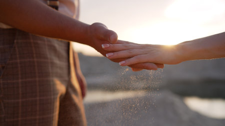A guy and a girl pour sand out of their hands. The concept of lost time, life. Sand through fingers close-up, against the backdrop of sunset.の写真素材