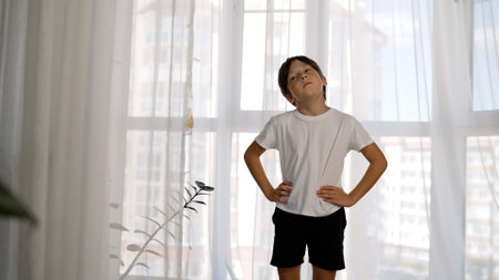 A boy does exercises in the morning at home. Little boy training at home. A boy does exercises for his neck while standing. A school-age boy performs head turning exercises.の写真素材