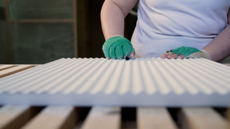 Hand sanding of wood panels, furniture production. A female carpenter works with wood in a carpentry workshop, sanding a wooden surface with sandpaper.の写真素材