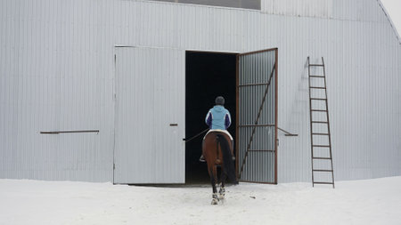 A girl on a horse enters the hangar for training in winter. Hangar for racing in winter. Girl rider...