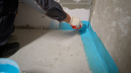 A person painting a wall with light blue paint. Applying blue waterproofing to a bathroom floor.の写真素材
