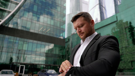 Businessman looks at his watch and looks up. Time is money. Close-up of a confident mature man in formal wear checking the time while looking at his watch with a building in the background.の写真素材