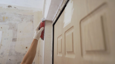 A worker manually polishes a white wall with a sanding sponge. Young adult man polishing a white wall with a sanding sponge by hand. Empty space for text. Concrete wall background, hand plastering with plastic sponge to finish cement wall.の写真素材