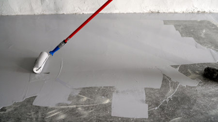 Applying paint with a roller to a concrete floor. A man paints a concrete floor with a paint roller. Varnishing of concrete floors. Apply primer to the surface using a roller brush. Close-up.の写真素材