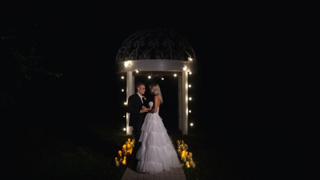 Tender and happy bride and groom on the evening street. Romantic walk and photo shoot in the dark. Night wedding ceremony. Young couple bride and groom on the street at night.の写真素材