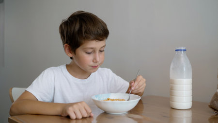 Beautiful boy, schoolboy preparing breakfast by pouring milk. Boy pouring milk for cereal into plate. Childrens breakfast. Boy pouring milk into plate to eat cereal.の写真素材