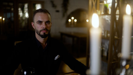 Young man waiting for dinner. Young man at a set table in a restaurant. Handsome man sitting with lit candles in a restaurant and waiting for his lady.の写真素材