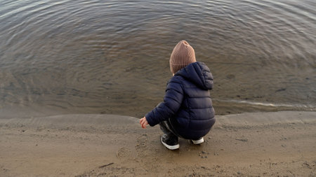 Young boy plays joyfully at the water's edge on a tranquil beach, enjoying the beauty of nature and...