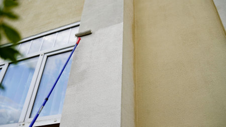 Construction worker painting a building using a paint roller on a telescopic handleの写真素材